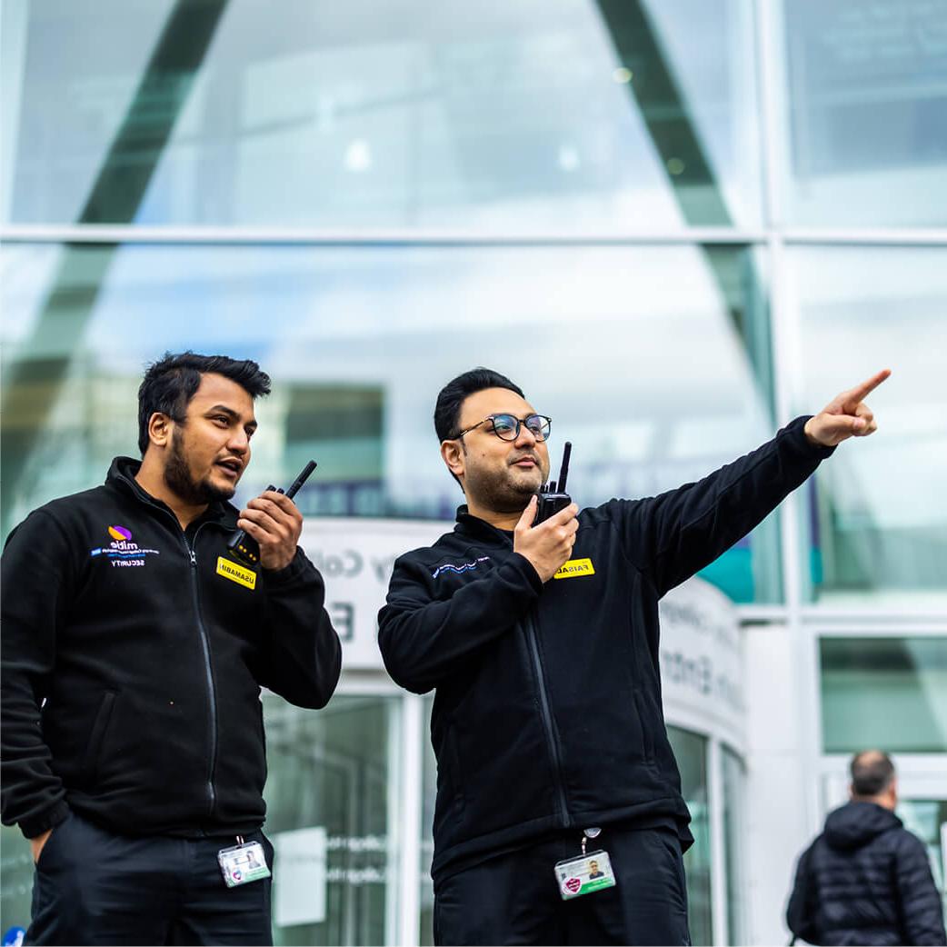 Two Mitie security guards standing and using walkie talkies outside a hospital